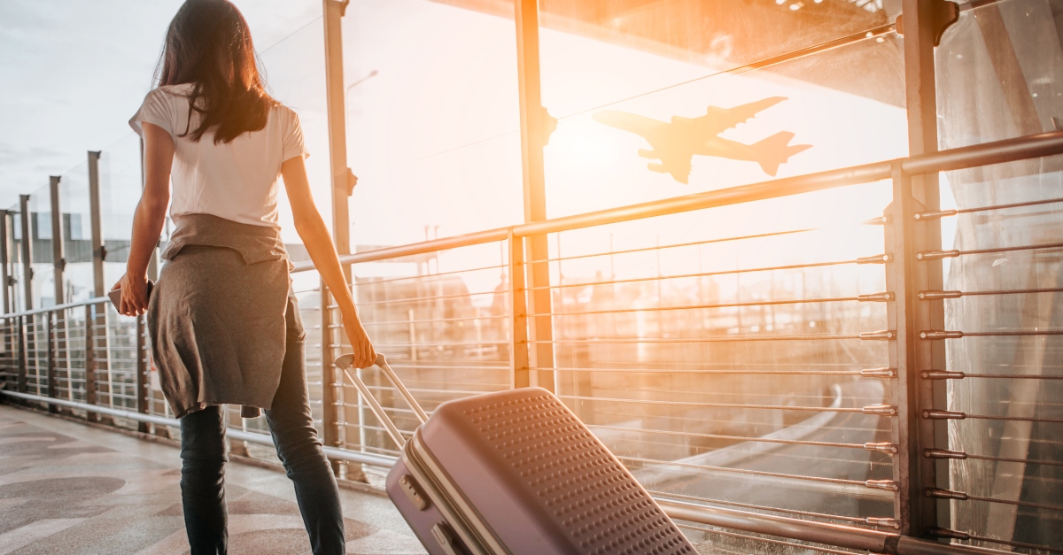 Young woman pulling suitcase in  airport terminal. Copy space