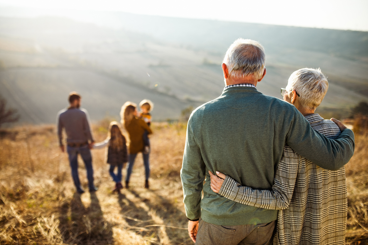 Rear view of embraced senior couple looking at their family in nature.