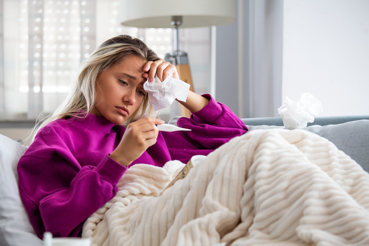 Sickness, seasonal virus problem concept. Woman being sick having flu lying on sofa looking at temperature on thermometer. Sick woman lying in bed with high fever. Cold flu and migraine.