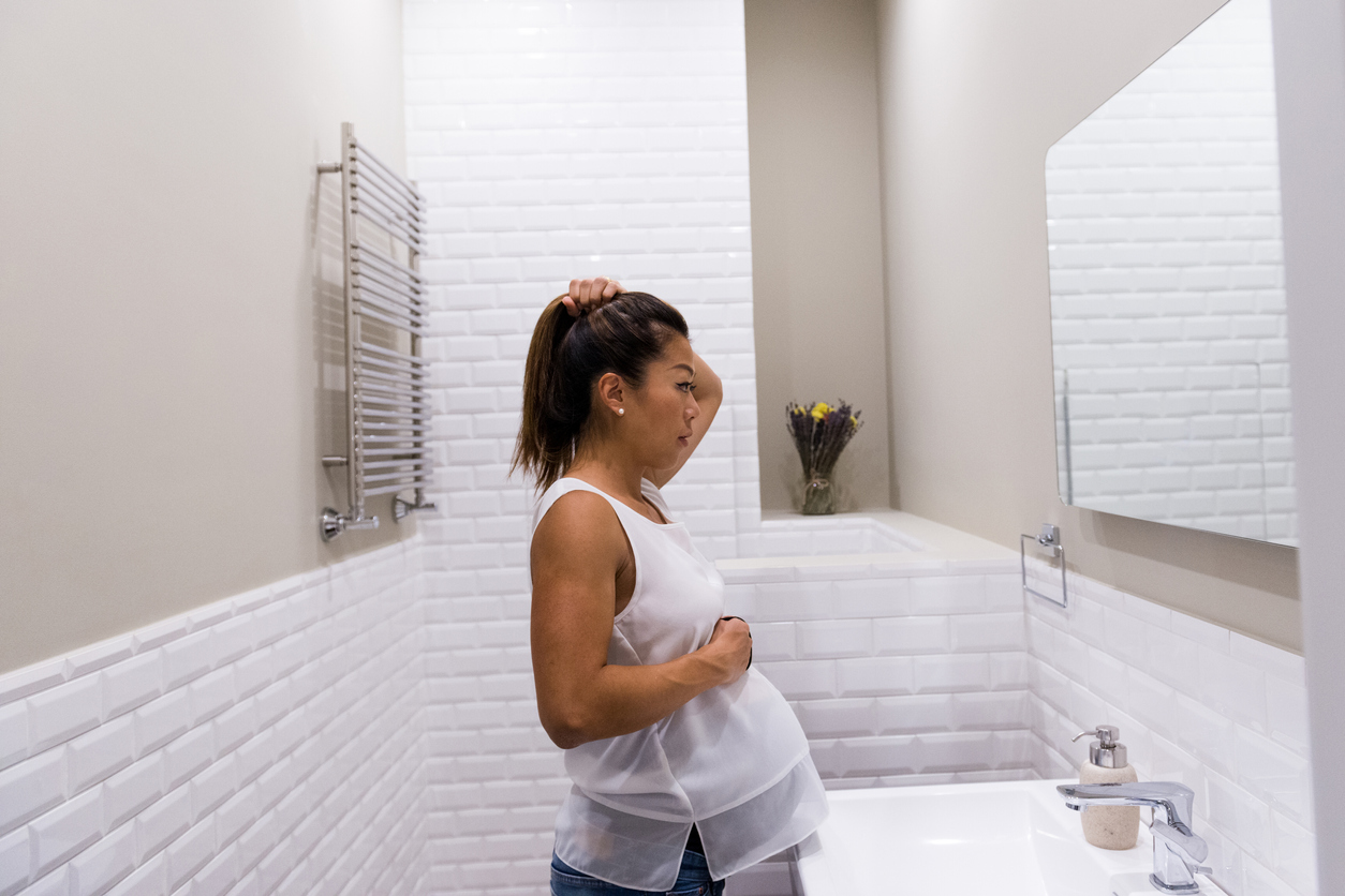 Mid adult pregnant woman fixes hair in bathroom mirror