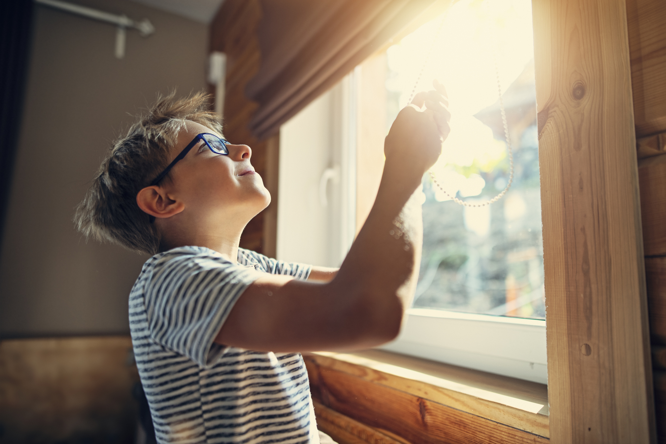 Little boy opening the roller blinds in the morning