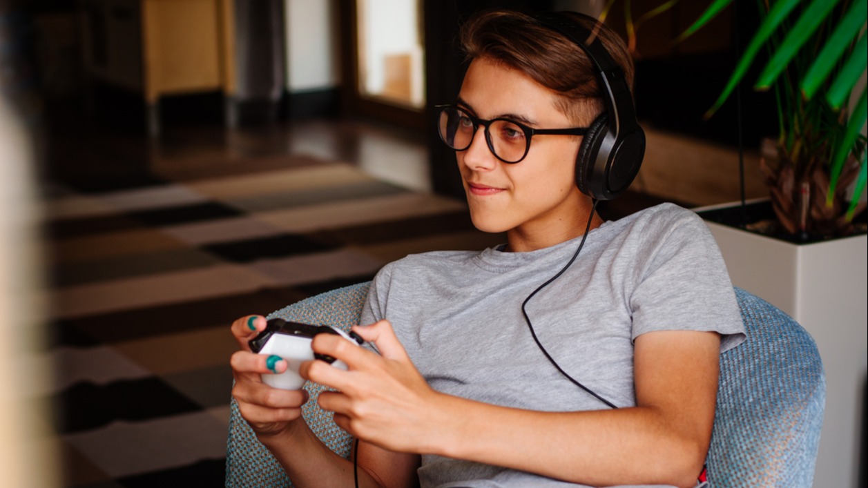 Smiling teenager boy in glasses and headphones playing game console