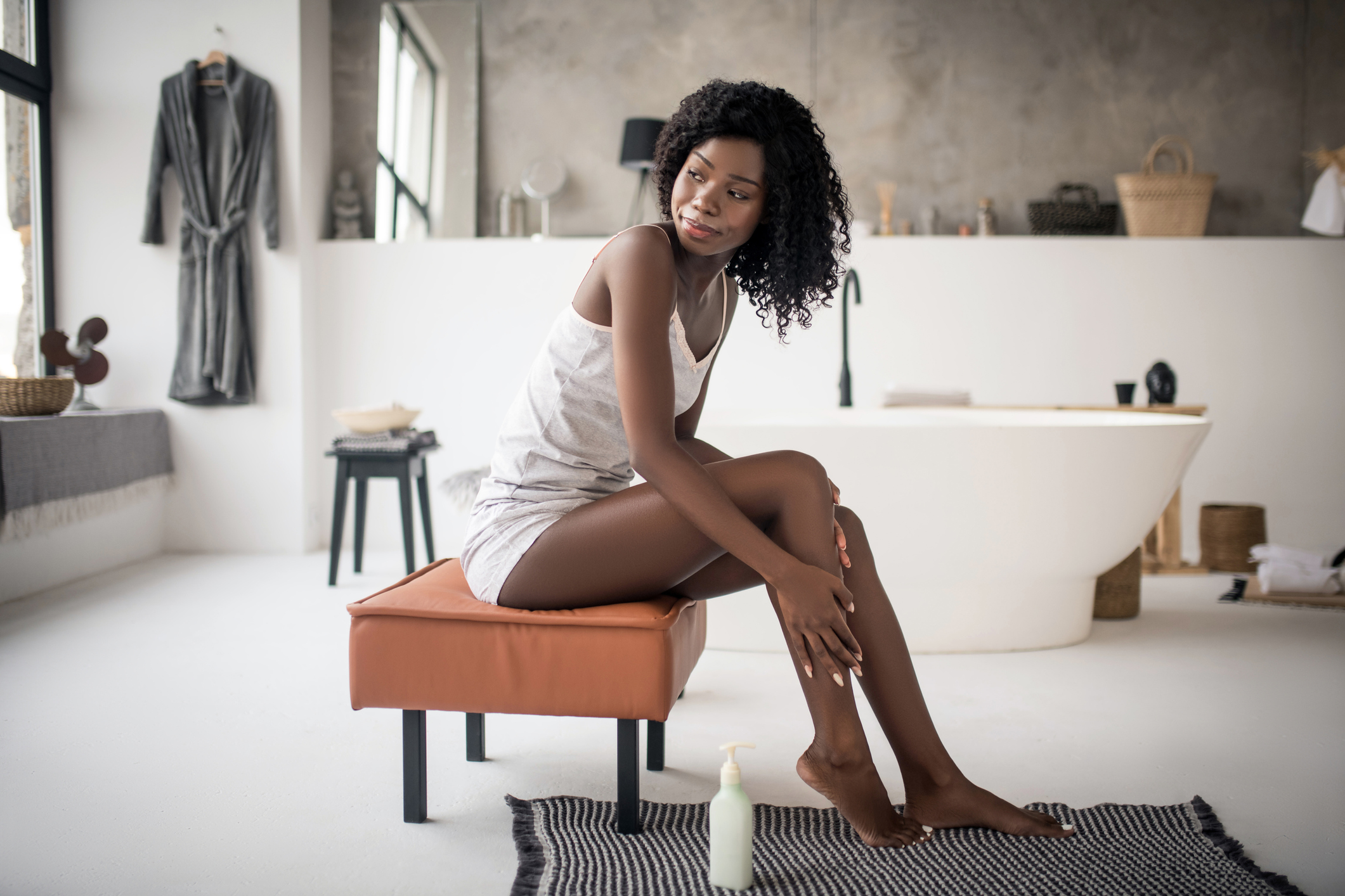 Curly woman sitting on chair and using cream after having bath