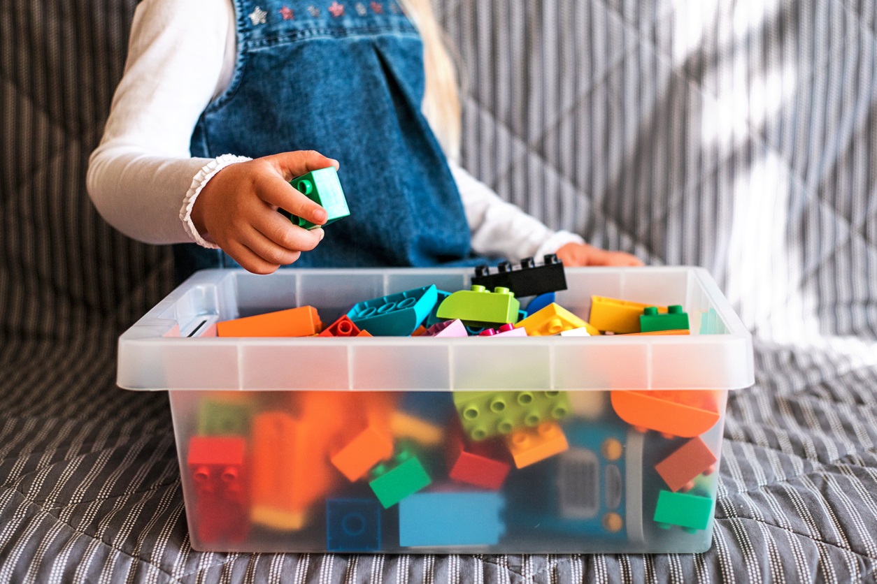 Little girl cleaning up the toy box at home.