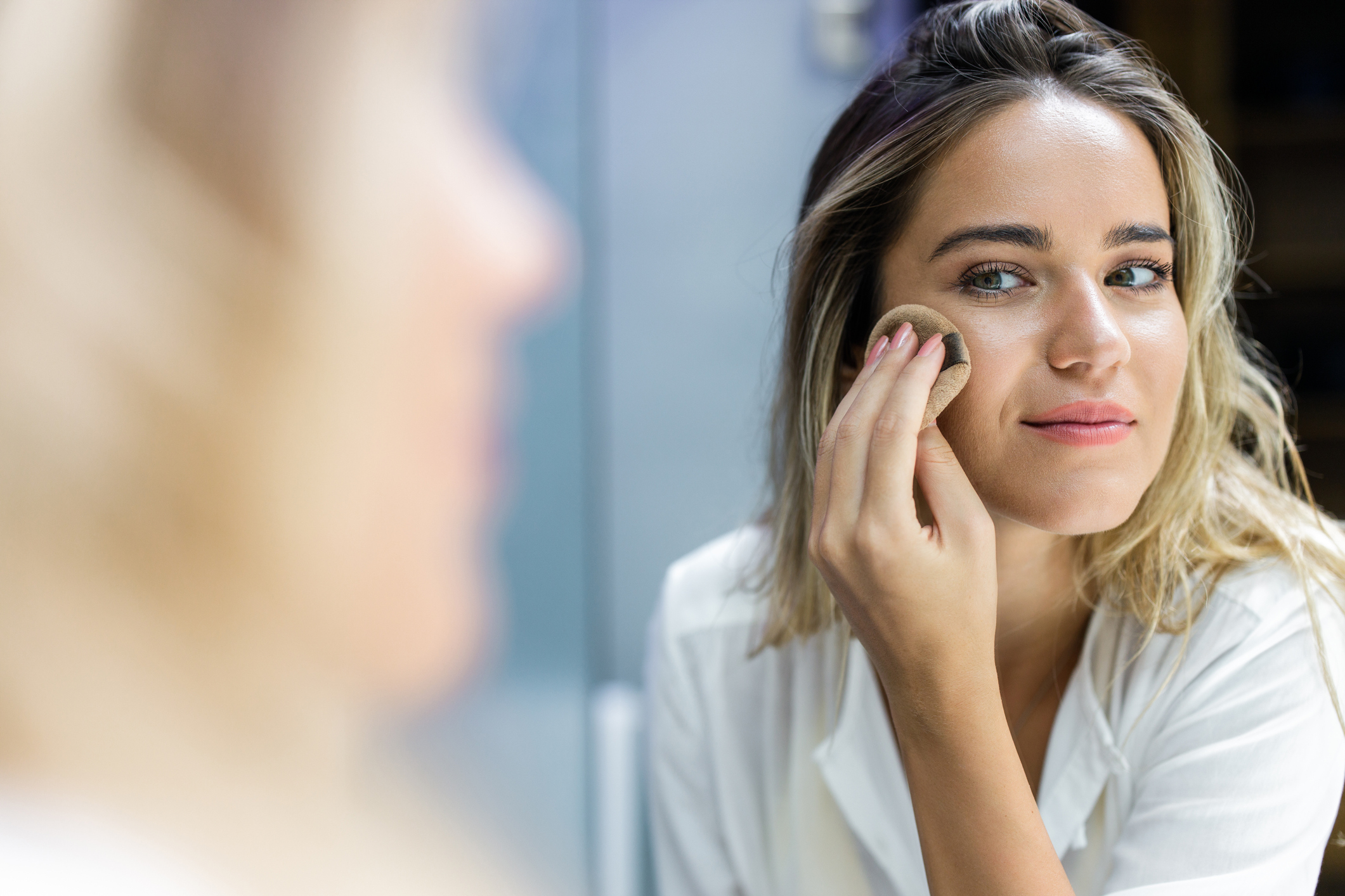 Reflection in a mirror of a woman applying face powder in bathroom.