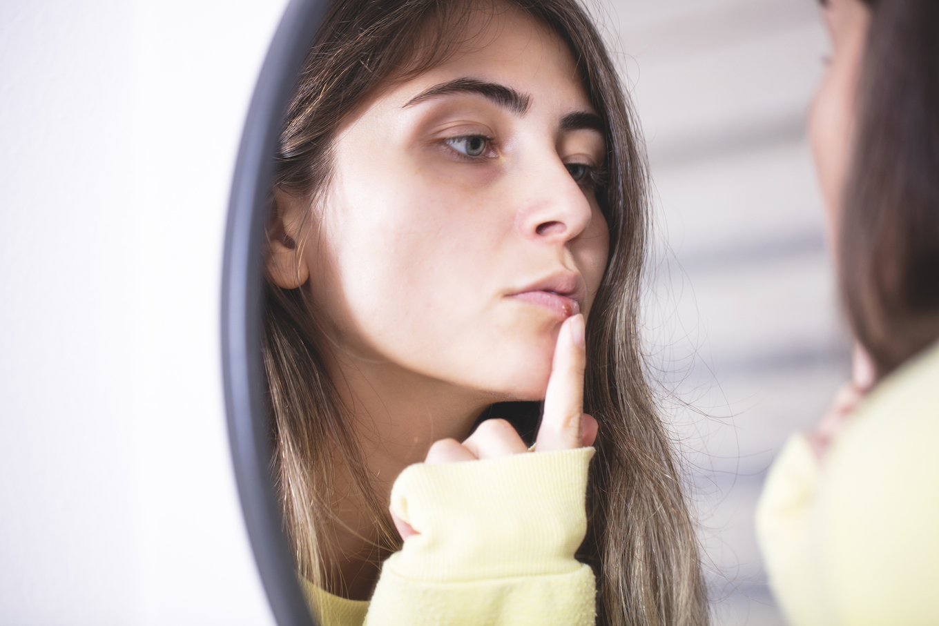 Woman applying cold sore cream on lips in front of mirror