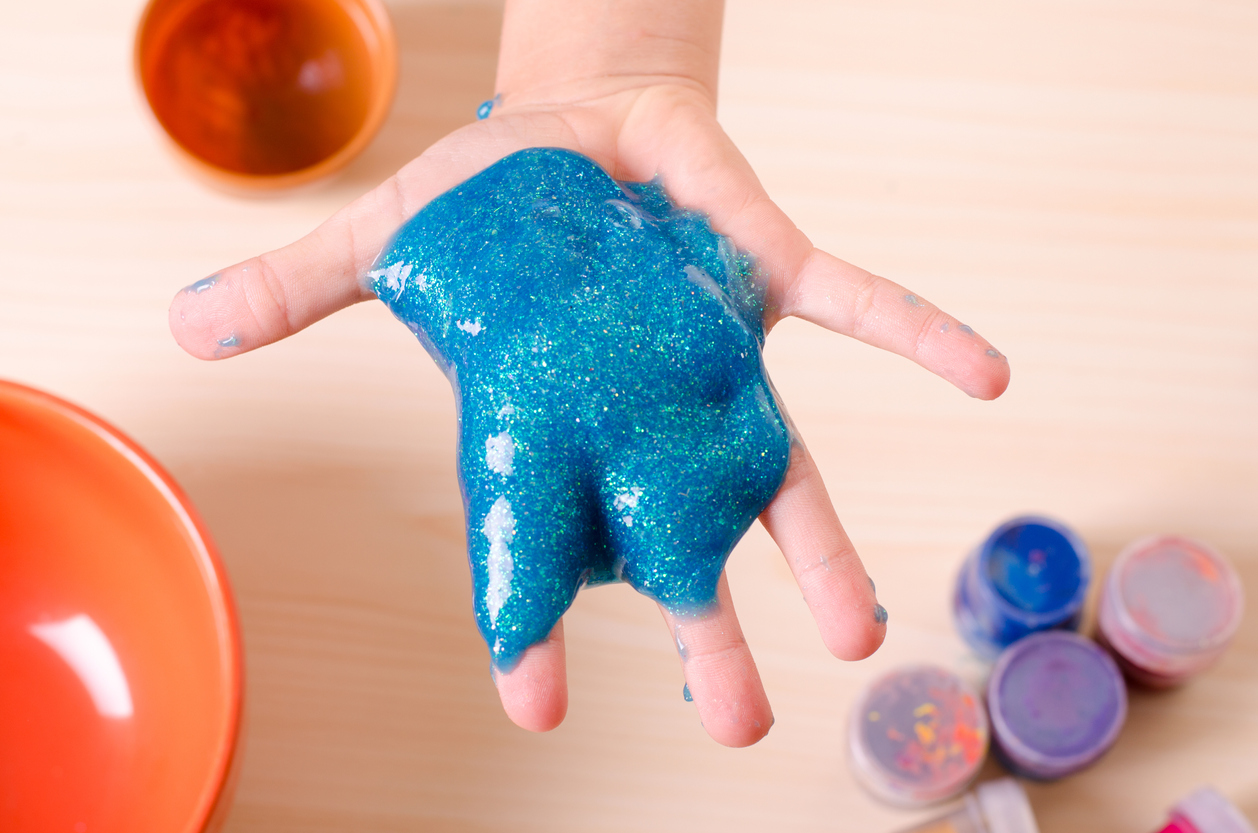 Child's hand holding bright glitter slime. Kid playing with slime, worldwide popular self made toy.