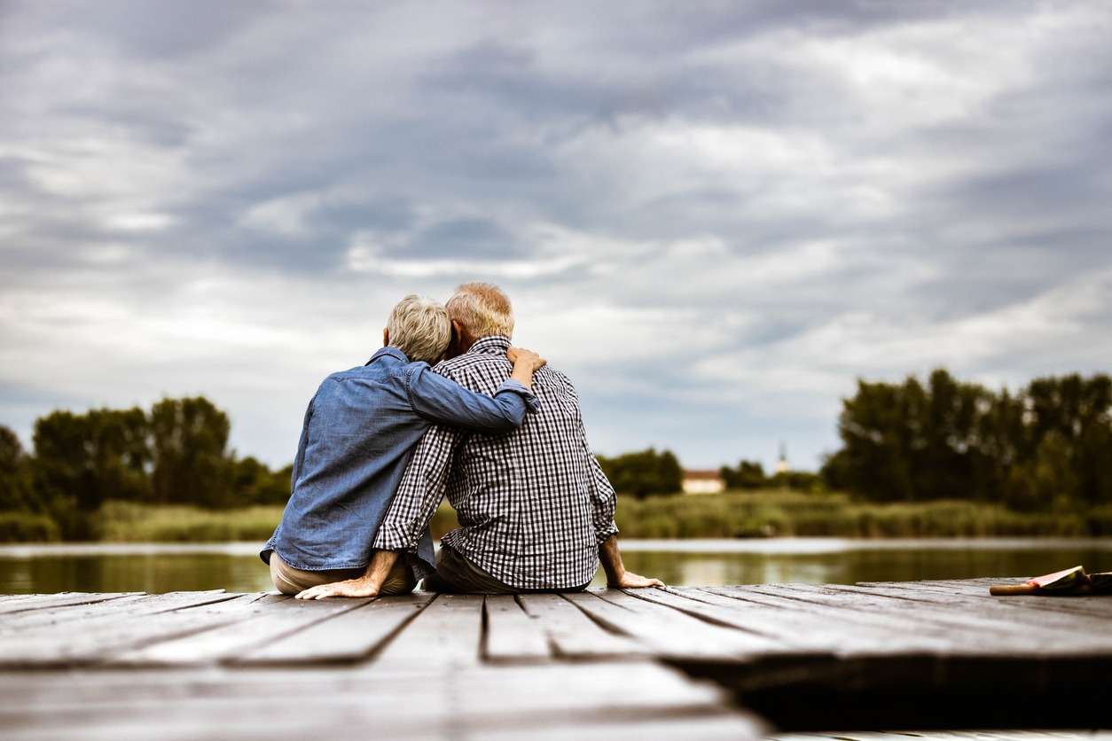 Rear view of a loving senior couple on a pier at river.