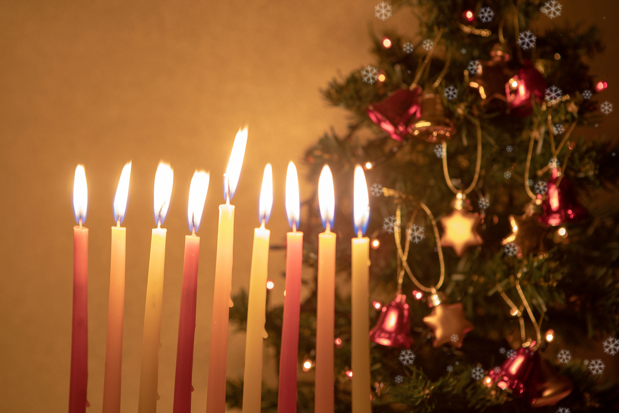 Hanukkah candles burning on the background of Christmas tree, decorated with snowflakes decoration