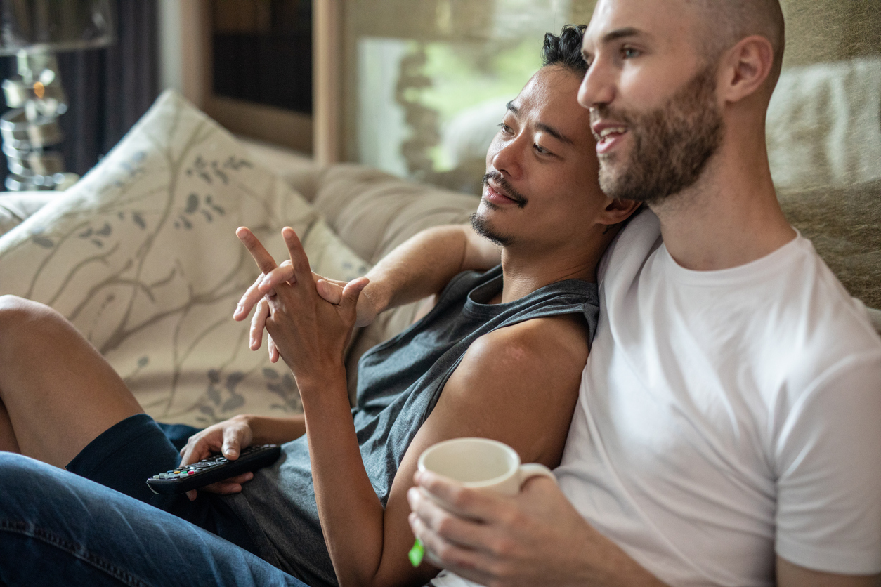 Gay couple relaxing on sofa and watching TV during weekend morning