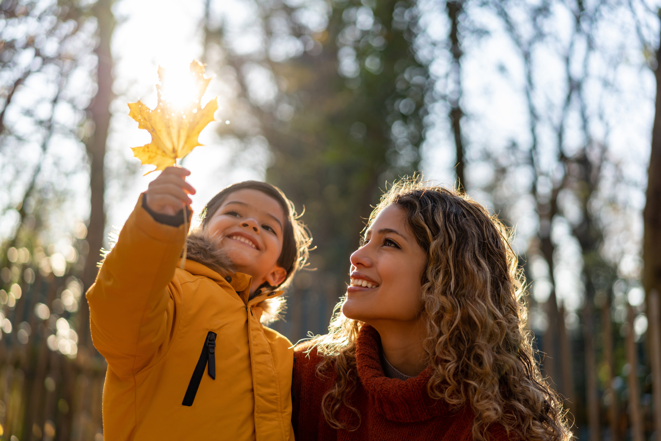 Beautiful mother looking at a leaf her son is holding on a sunny autumn day at the park