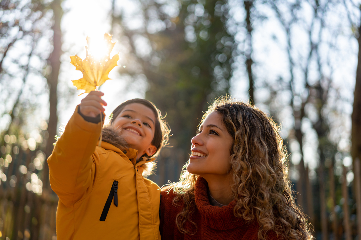 Beautiful mother looking at a leaf her son is holding on a sunny autumn day at the park