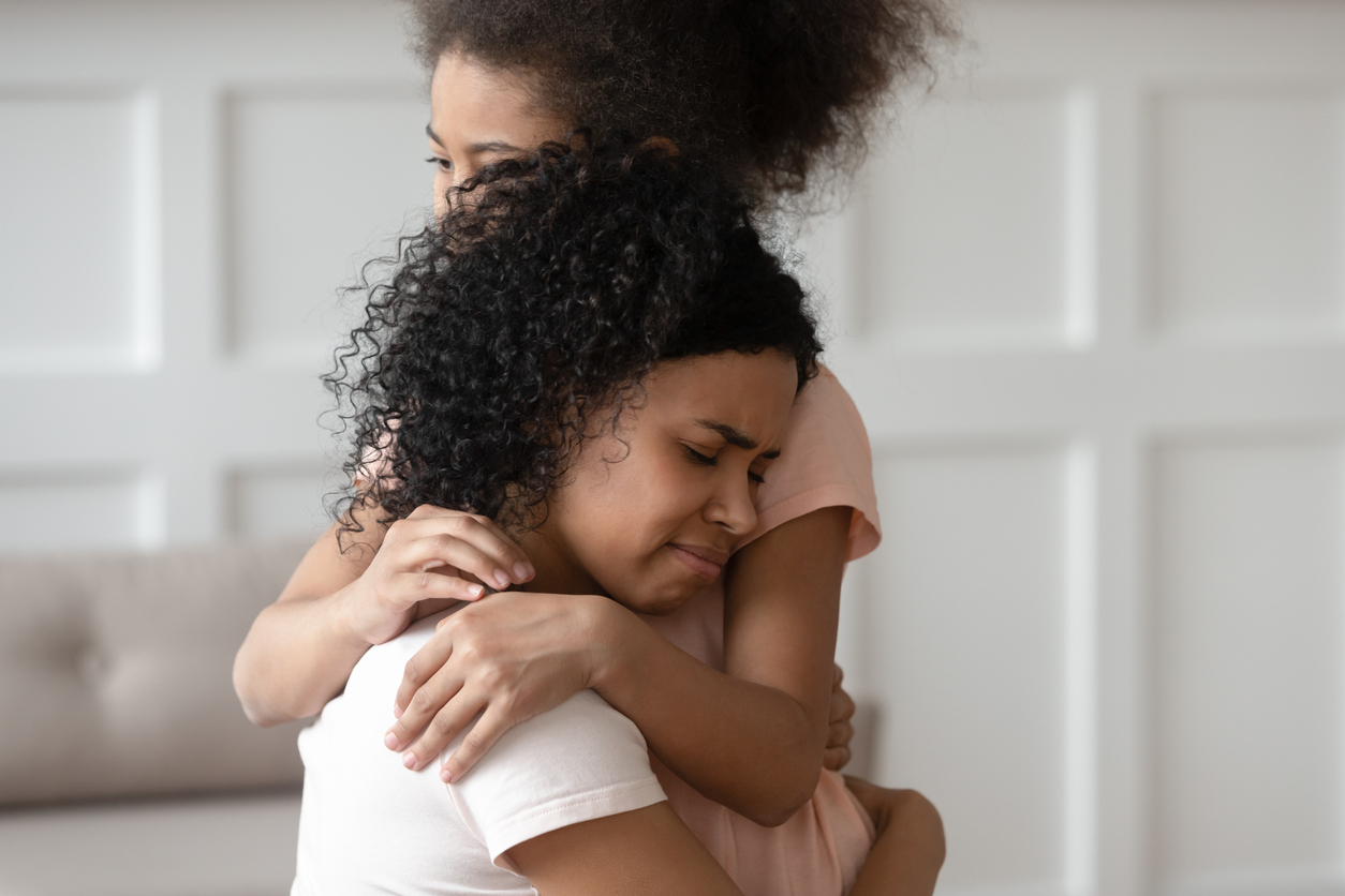 Close up sad upset black woman cuddling daughter.