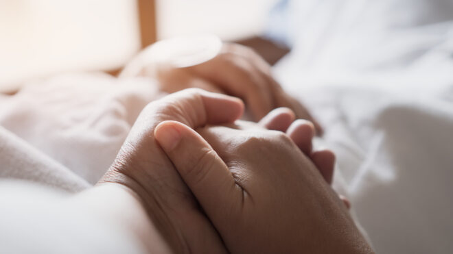 Holding patient's hand in hospital bed