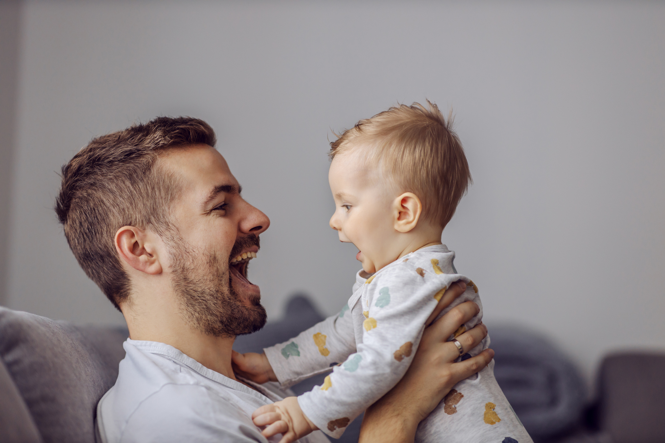 Adorable little blond boy playing with his caring father and biting his nose. Father is smiling.