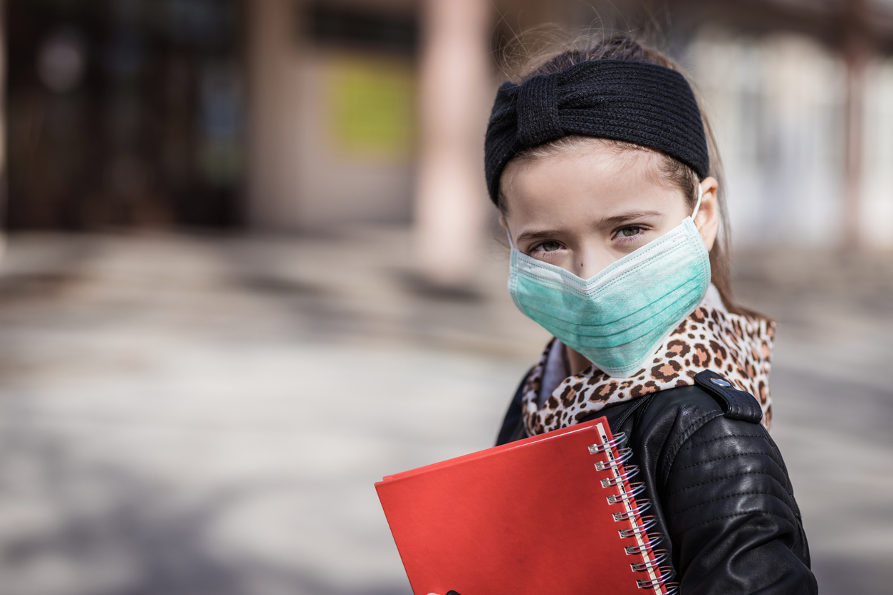 Young child holding notebook and wearing medical face mask