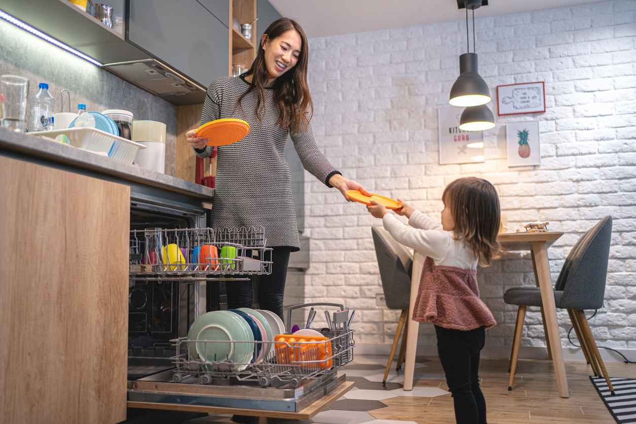 Cute toddler helping mother with the dishes at home