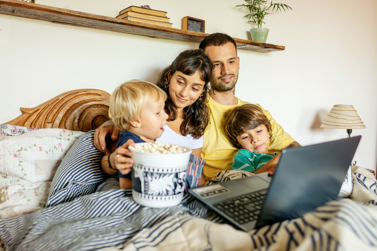 Family watching movies in the laptop lying in the bed and eating popcorn