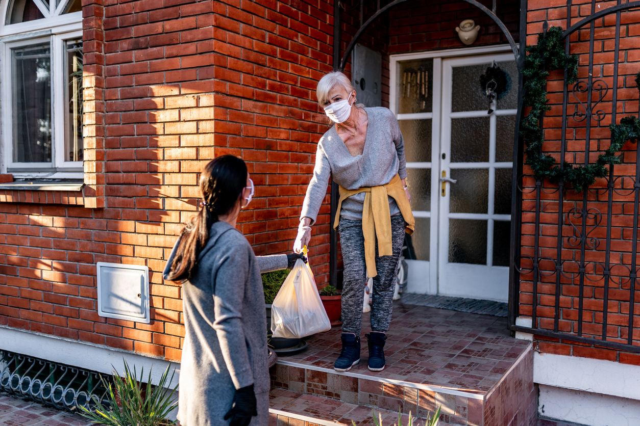 Female volunteer bringing groceries to a senior woman at home