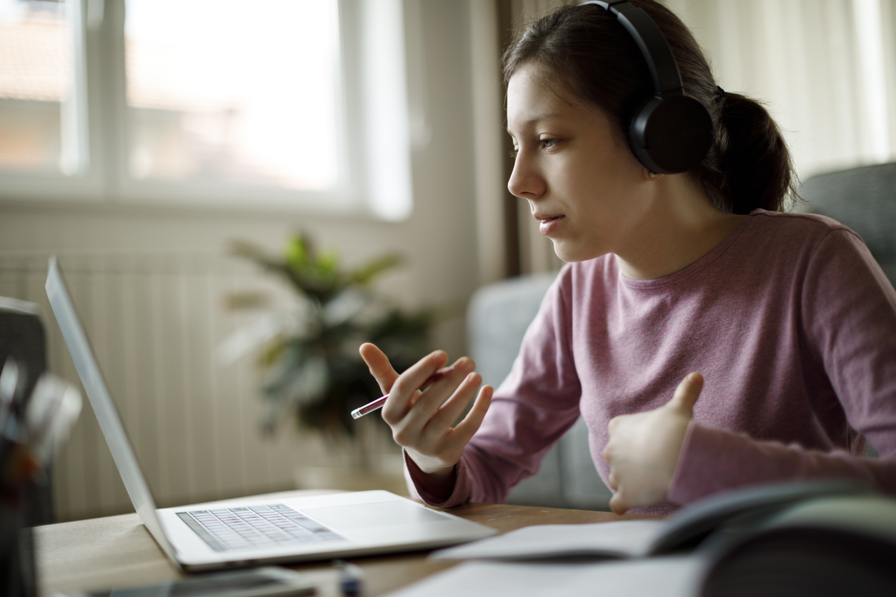 Teenage girl with headphones having online school class at home