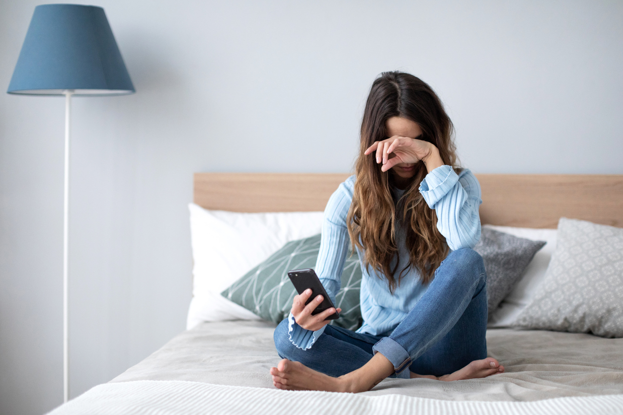 Angry young  woman with a mobile phone in casual wear on a sofa at home.