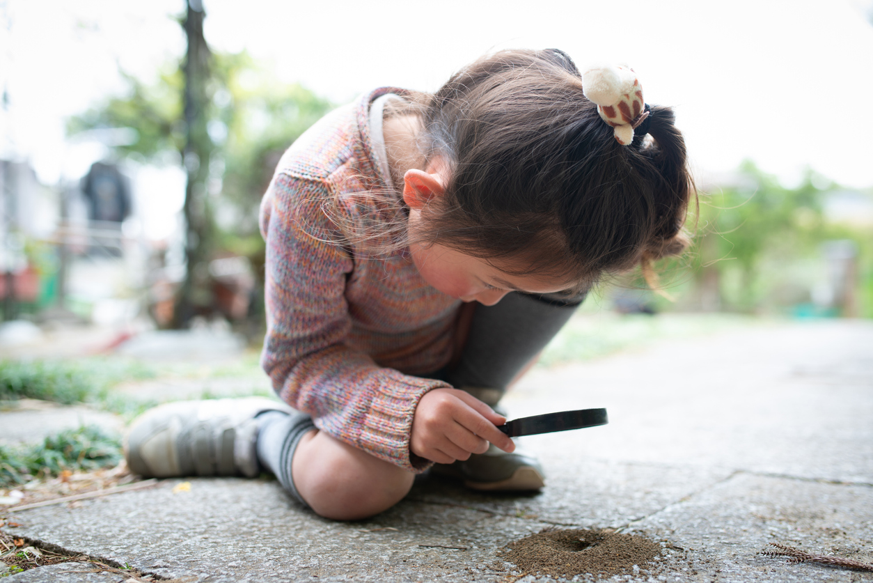 Girl observing ant nest with magnifying glass