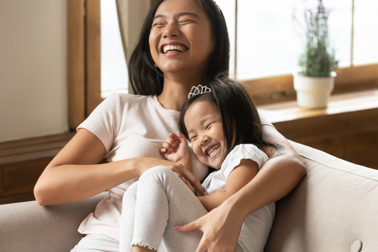 Overjoyed asian mother tickling little daughter having fun at home