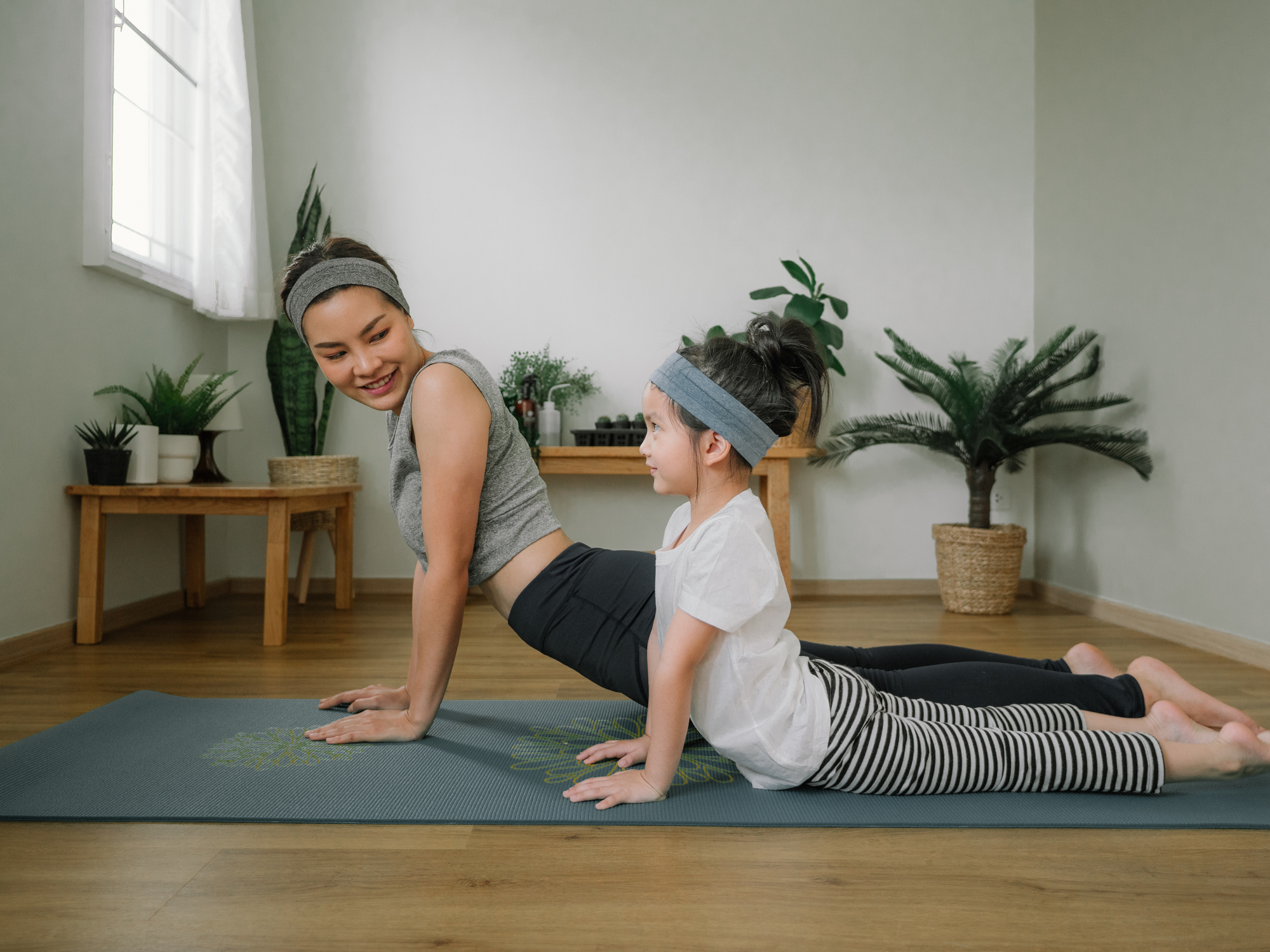 Mother doing on yoga mat with little daughter at home.