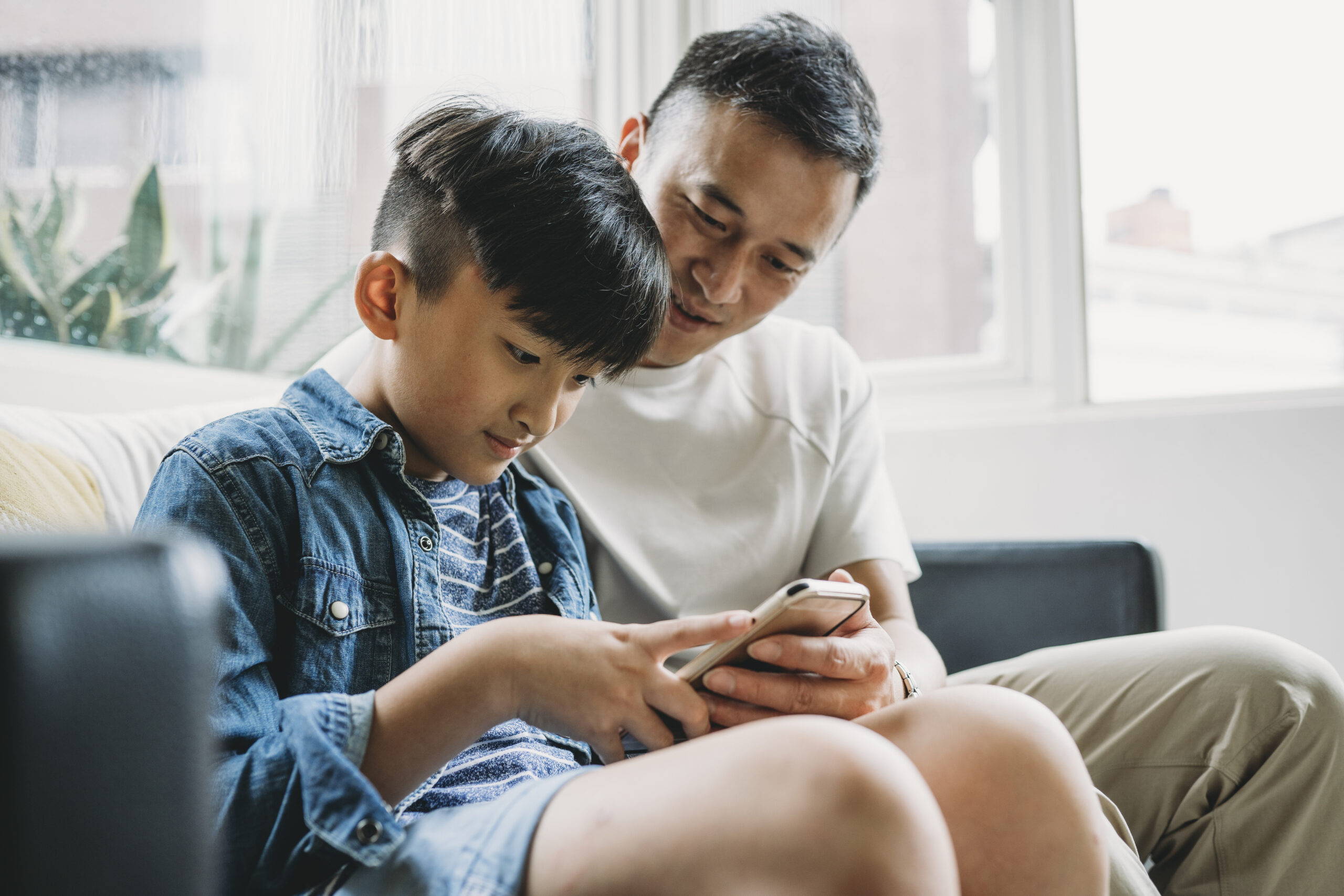 Father and son using a mobile phone together sitting on the sofa at home