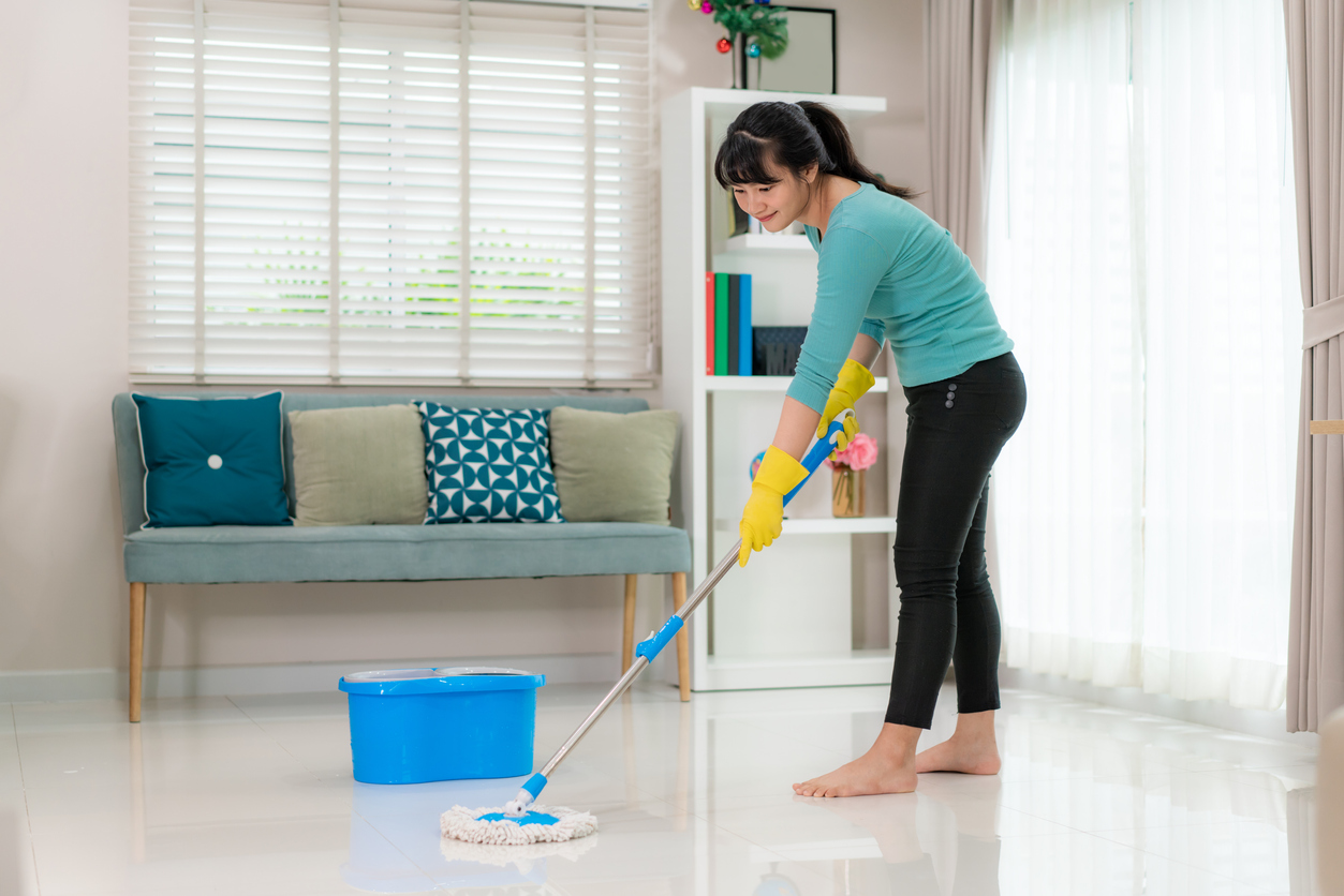 Attractive young Asian woman mopping tile floor at living room while doing cleaning at home during Staying at home using free time about their daily housekeeping routine.