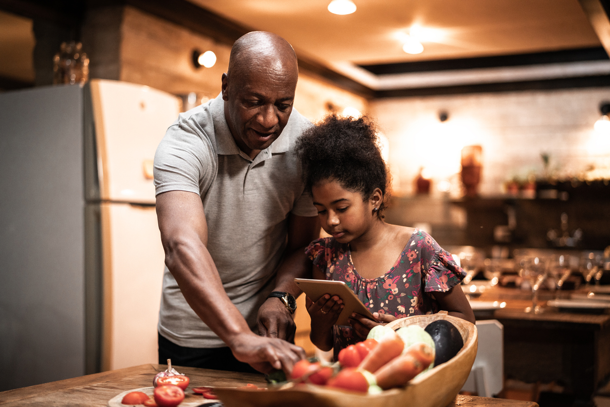 Grandfather and granddaughter cooking at home using digital tablet