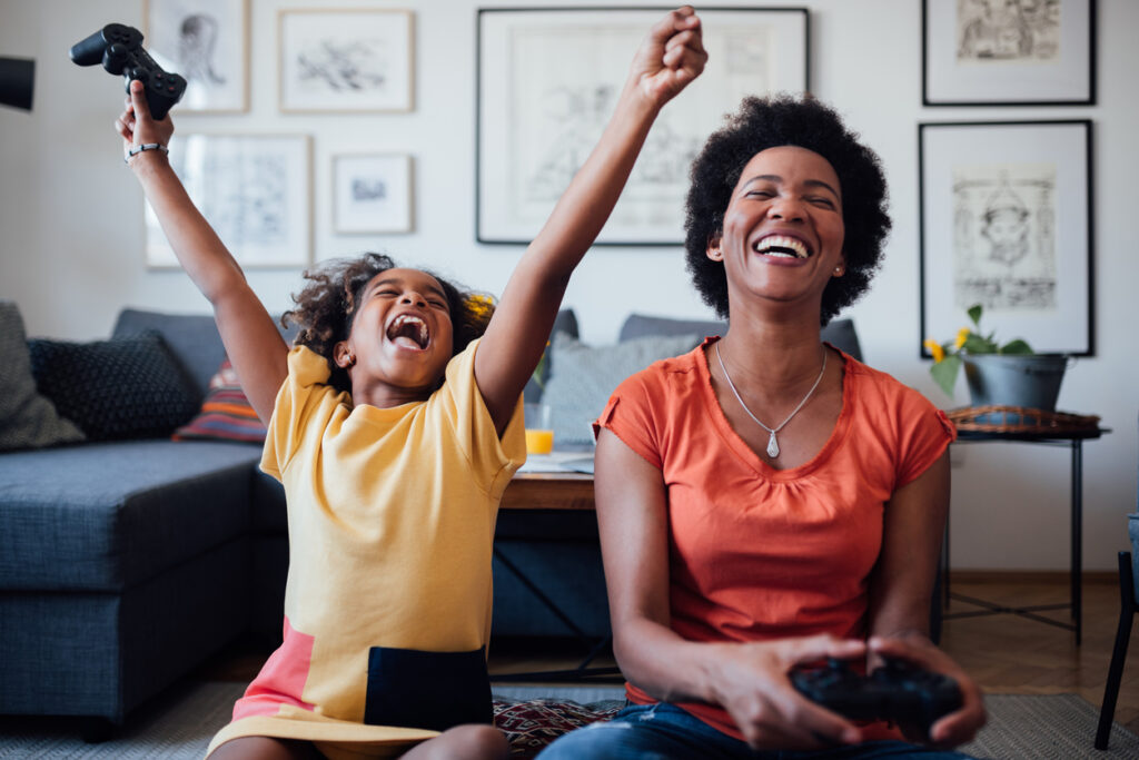 Young little African American girl with her African American mother spending some quality time together at home playing video games and having fun