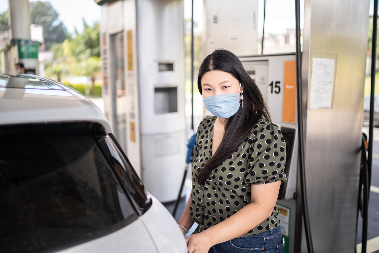 Portrait of young woman with face mask refueling her car at a gas station