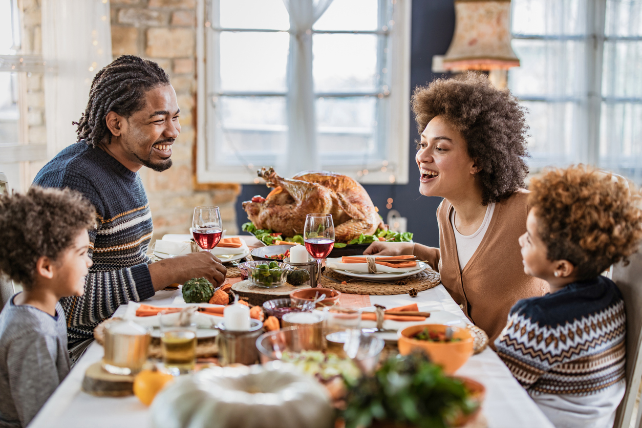 Happy black family talking during Thanksgiving meal at dining table.