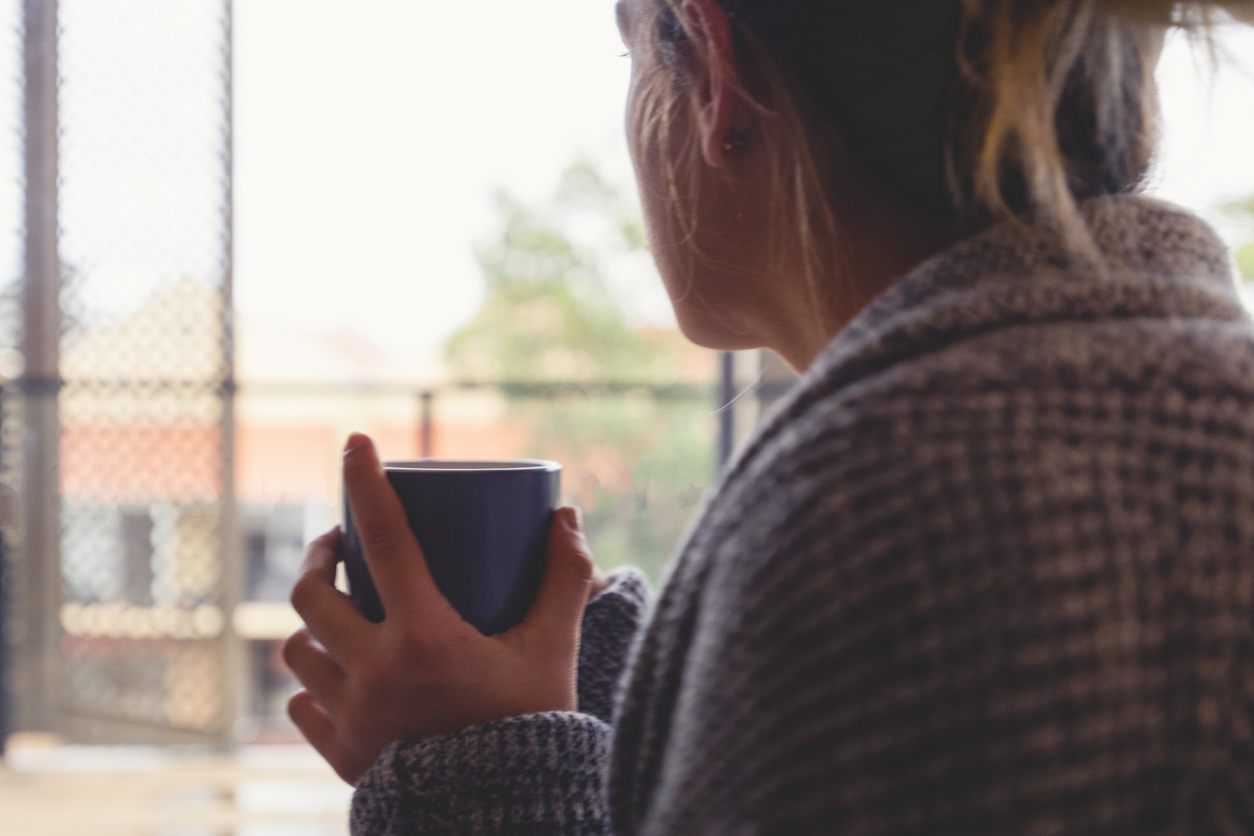 Woman looking through the window drinking tea or coffee.