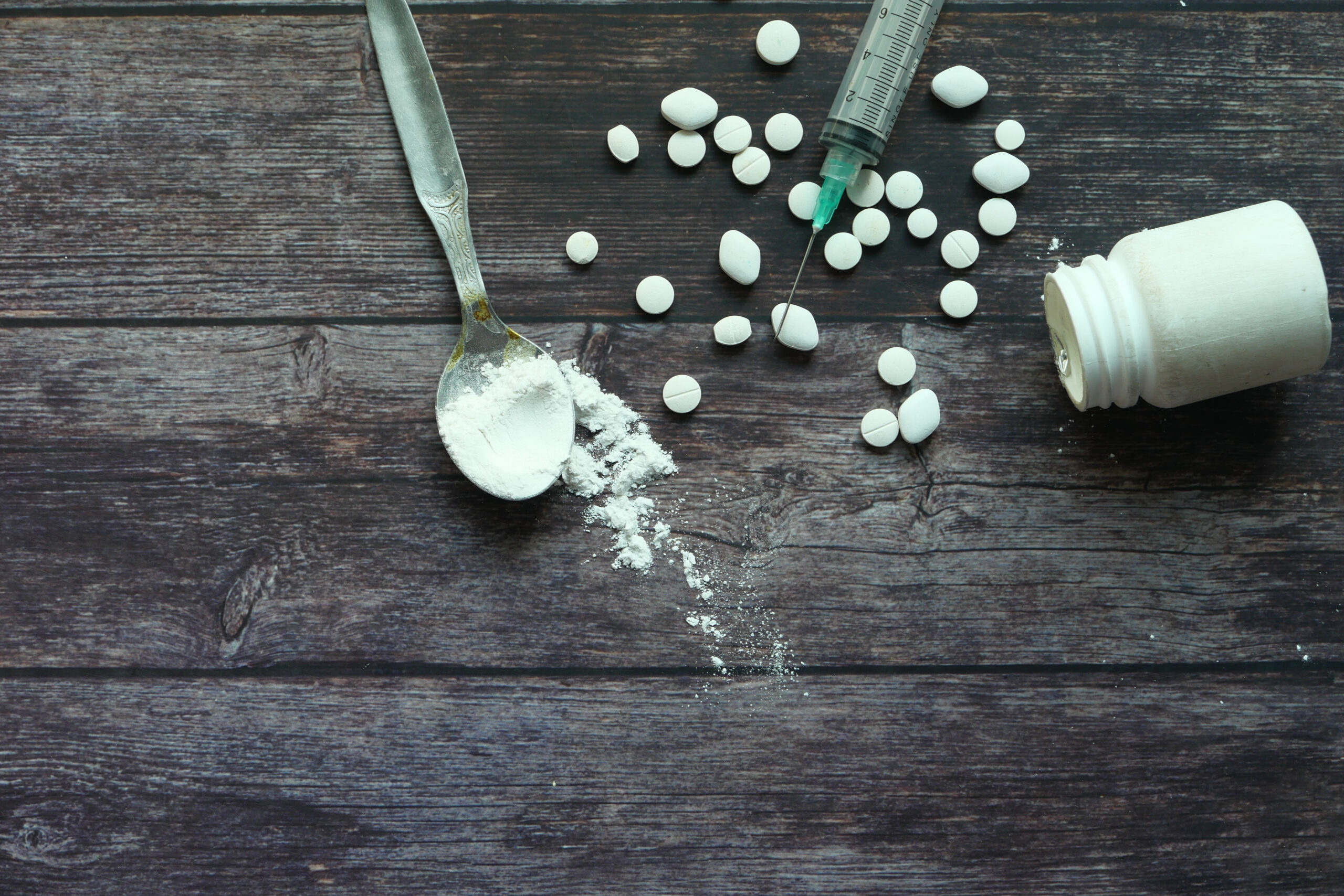 Heroine, syringe and pills on wooden background