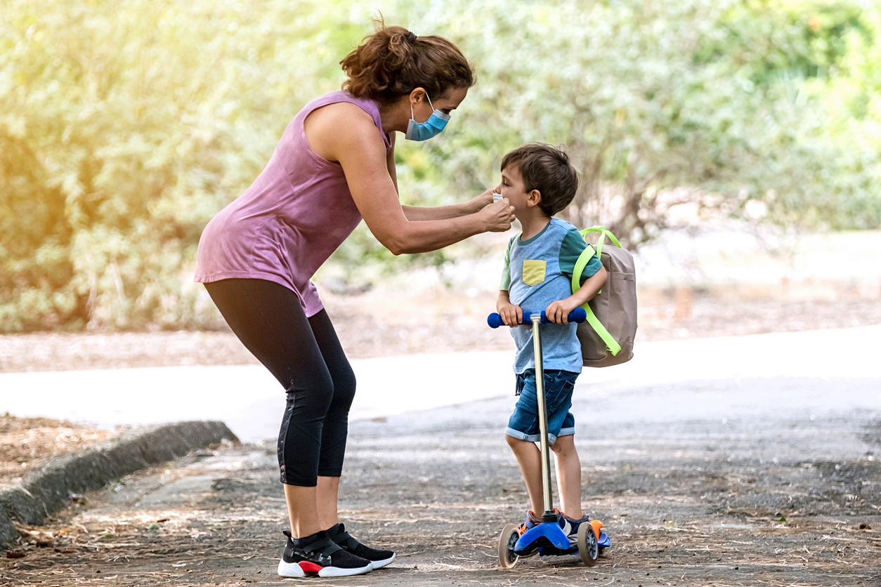 Mature woman helping her son to wear a protective face mask before going to school