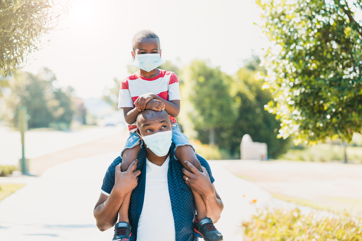 Dad gives son piggy back ride; both wear masks