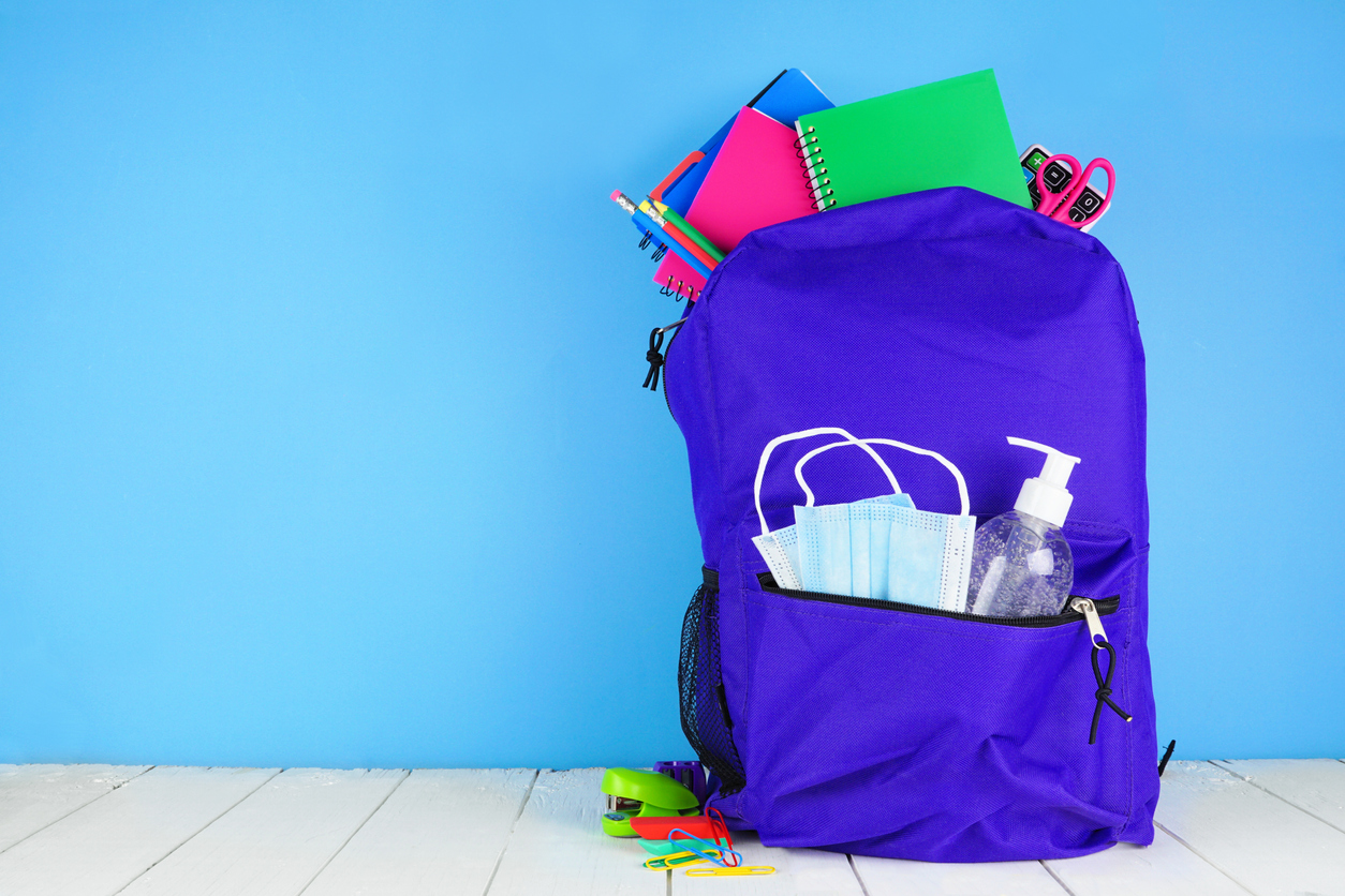 Backpack full of school supplies and COVID 19 prevention supplies against a blue background