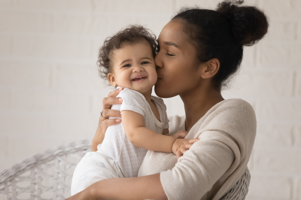 Close up loving young African American mother kissing toddler daughter