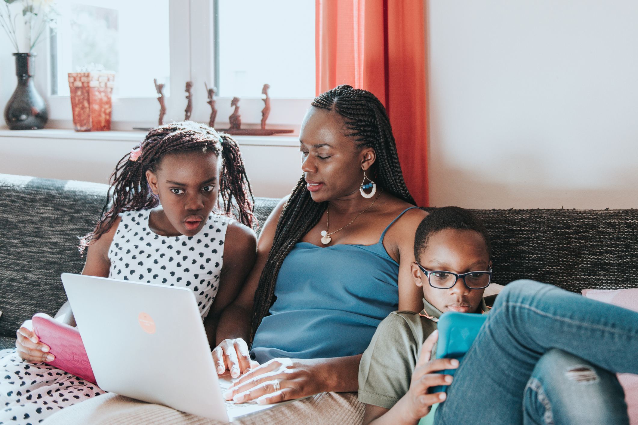 little girl and boy looking at their digital tablet while mother working at laptop on sofa