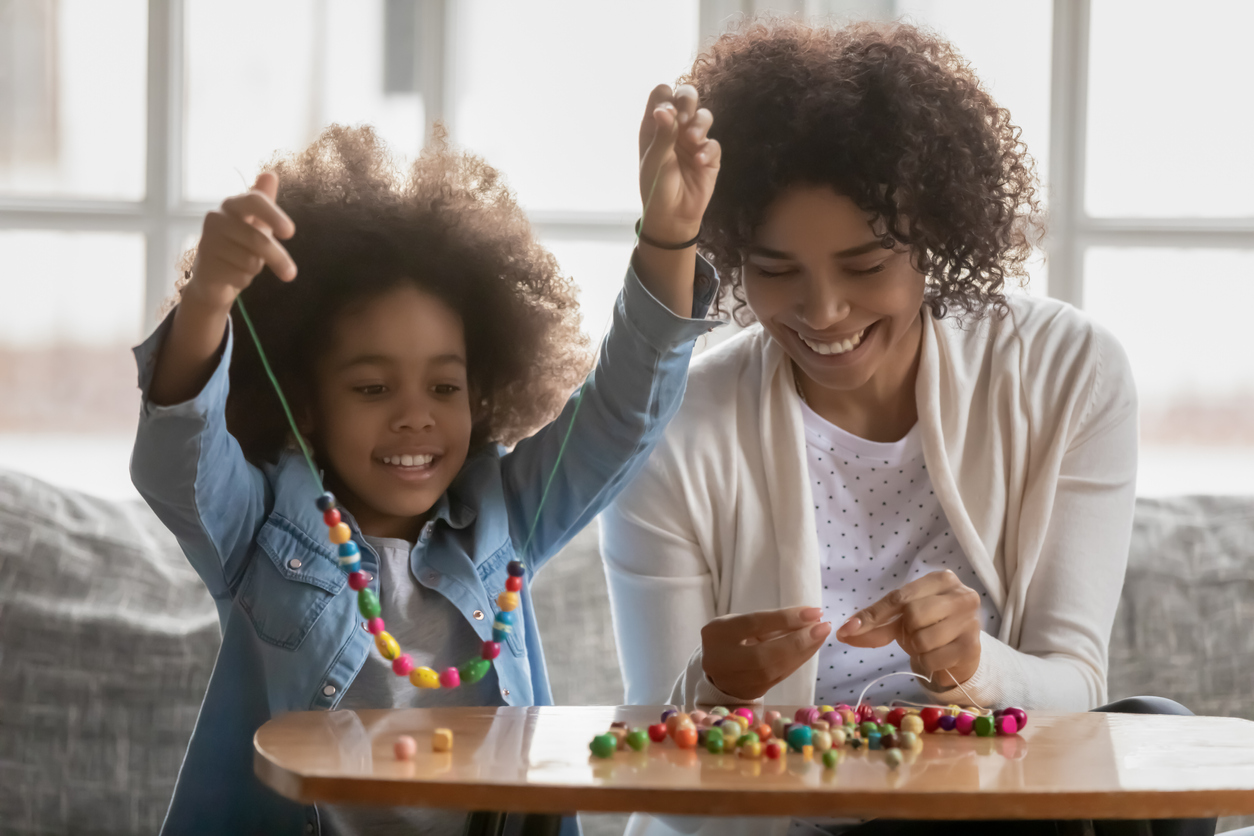 Happy biracial mother and little daughter make bracelets