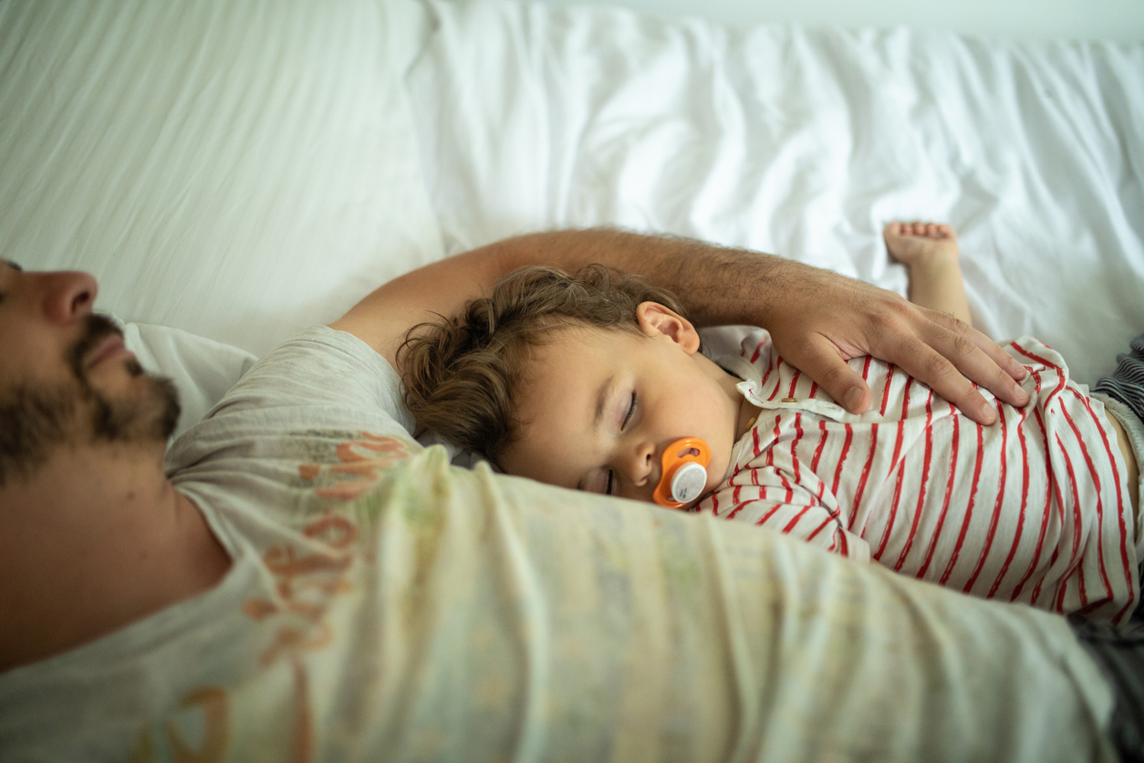 Toddler and his father napping on bed together