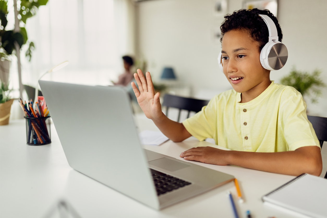 African American boy using laptop and waving during video call while homeschooling.