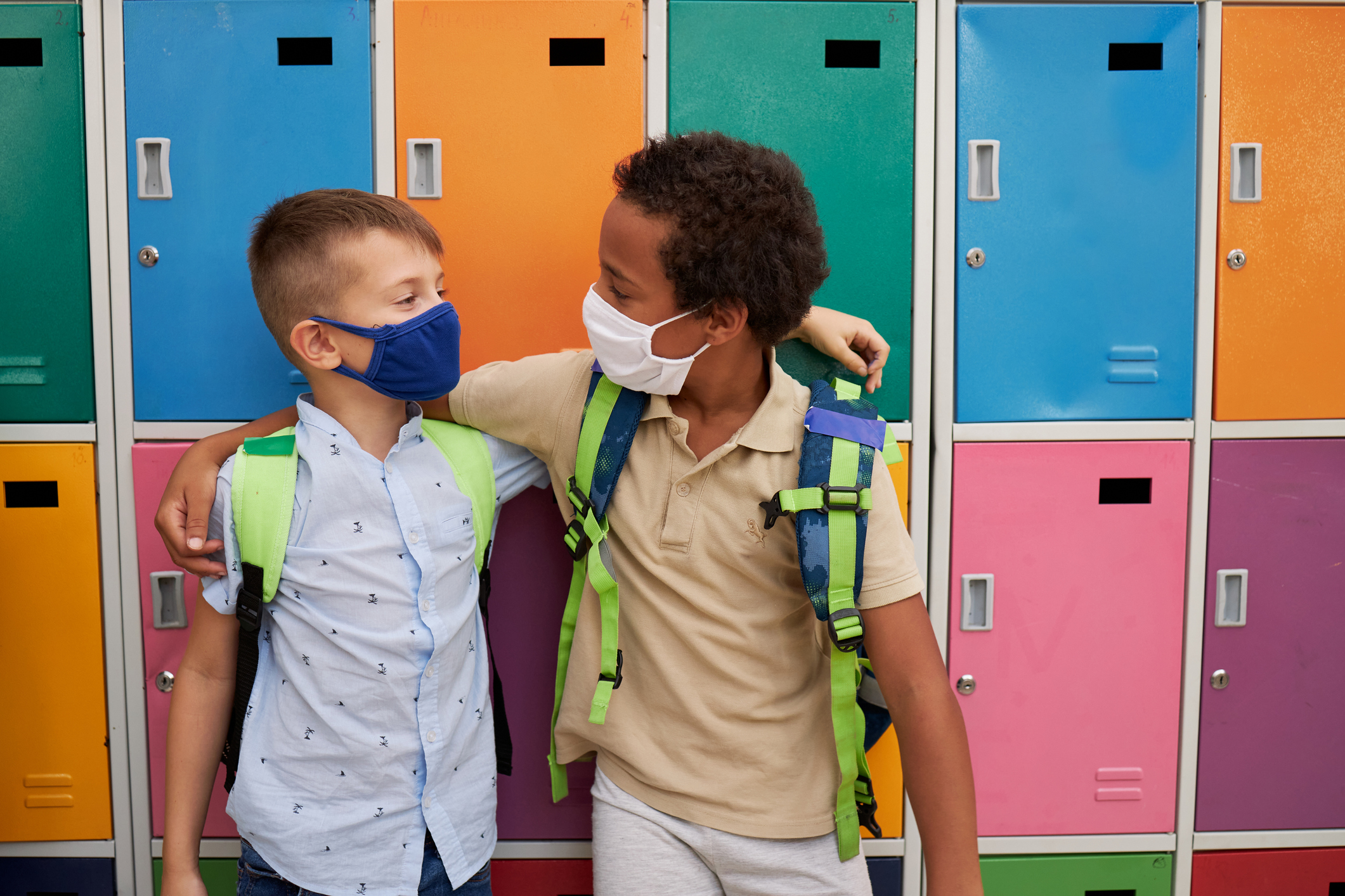 Happy multi ethnic male friends hugging while wearing protective face mask in the school