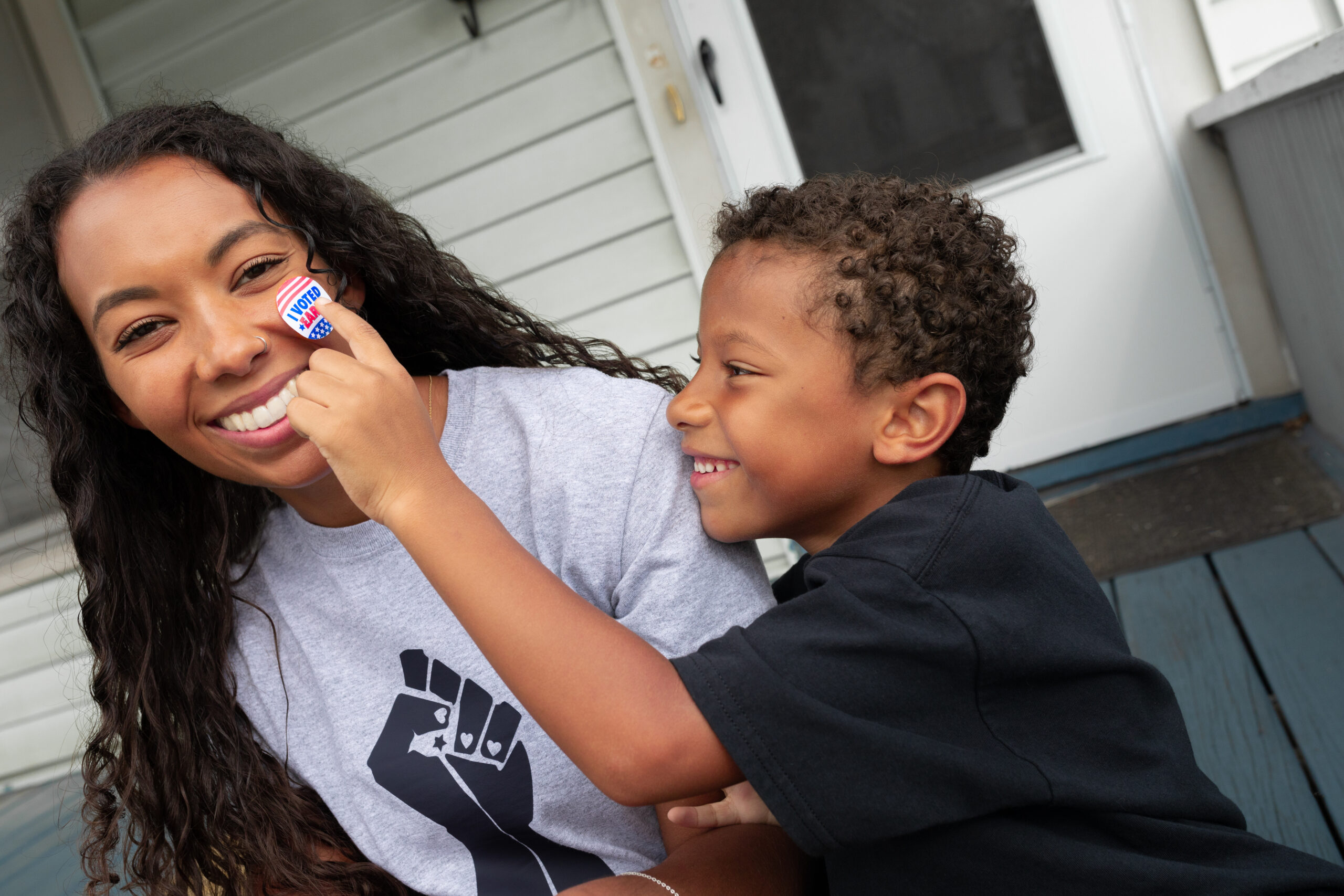 African American son placing I Voted Early Sticker on smiling black mother's face