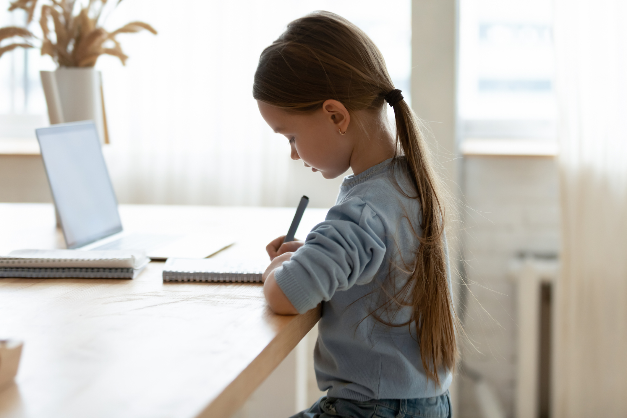 Focused small adorable caucasian girl preparing homework alone.