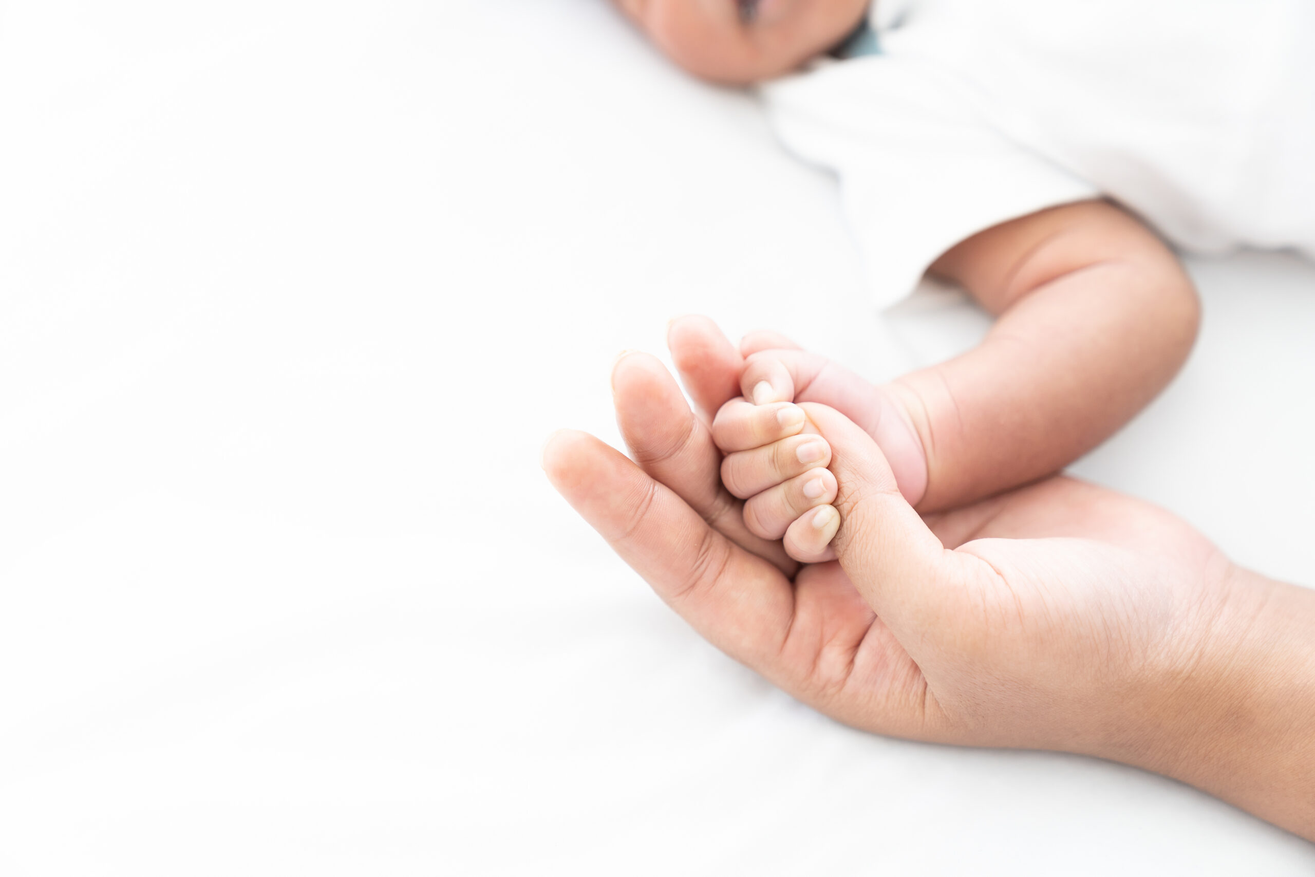 Newborn baby holding motherâs finder while sleeping on white bed. Mother takes care and comforting for her baby