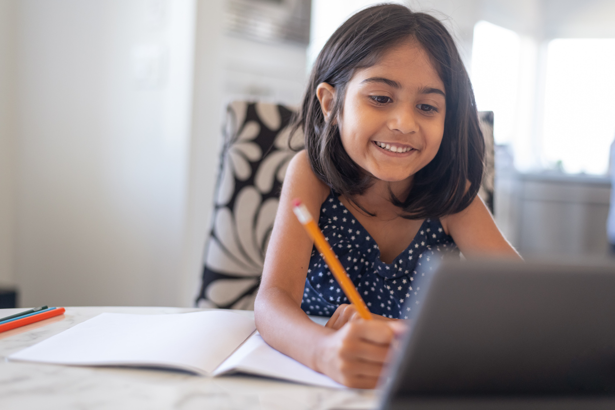 Cute elementary age girl using laptop computer while attending school online