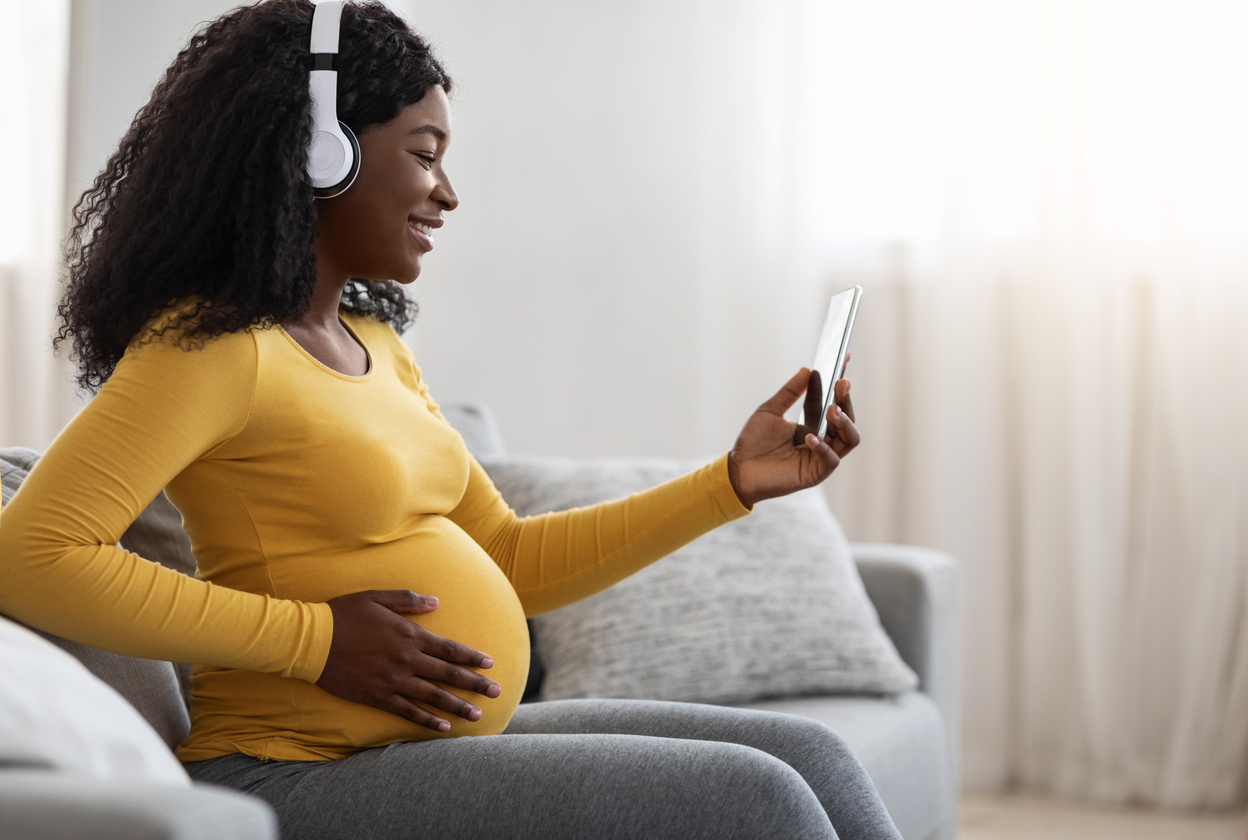 Pregnant black lady enjoying music, using mobile app